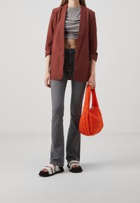 Maronroter Blazer, graues Cropped-Top, graue ausgestellte Jeans, schwarze Sandalen mit weißen Riemen und eine orange gesteppte Tasche. Glatte Texturen und kontrastierende Farben.