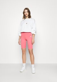 Calções de bicicleta rosa com cintura alta e riscas brancas laterais, combinados com um sweatshirt cropped branco e ténis brancos.