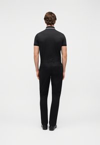 Μαύρο πόλο μπλουζάκι με λεπτομέρεια λευκού γιακά, συνδυασμένο με μαύρο παντελόνι και παπούτσια. Το ύφασμα φαίνεται λείο με εφαρμοστή σχεδίαση.