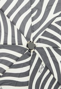 Ombrello pieghevole con un motivo a strisce zebra grigie e bianche, dotato di un pulsante nero al centro e di un tessuto testurizzato.