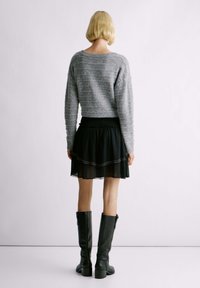 Maglione lavorato a maglia grigio chiaro con una vestibilità rilassata, abbinato a una gonna in chiffon nera a più strati con unince prima decorativa. Stivali neri in pelle al ginocchio.