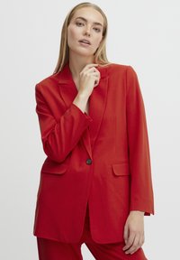 Blazer rosso con maniche lunghe, chiusura con un bottone, rever a toppa e due tasche frontali. Texture liscia, taglio sartoriale.