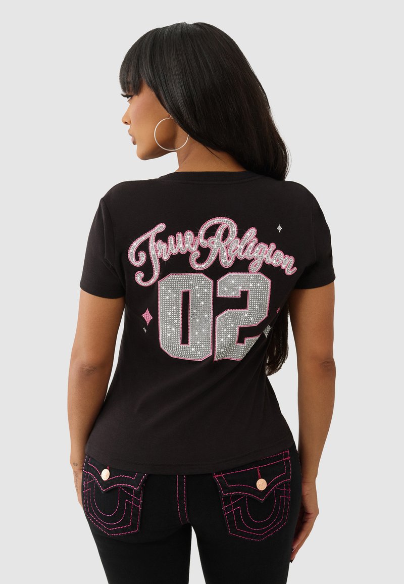T-shirt noir avec "True Religion" en paillette rose et argent, et le numéro "02" en strass. Manches courtes et col rond.