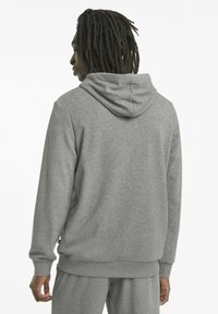 Sudadera gris con capucha, con puños y dobladillo acanalados. Tejido suave y texturizado, corte relajado y detalles de costura visibles.