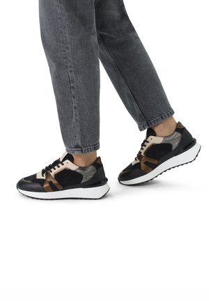 Black and brown athletic shoes with a mix of leather and suede, featuring a white sole and black laces, viewed from the side on a person.