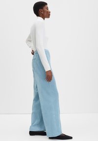Pantalon en velours côtelé bleu clair à jambes larges et ceinture élastique, associé à un haut ajusté à manches longues blanc et des chaussures plates noires.