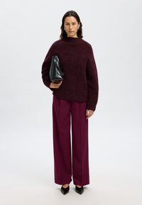 Pull bourgogne oversize avec un col haut, associé à un pantalon bourgogne à jambes larges. Sac à main noir structuré et chaussures noires à bouts pointus.