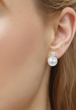 Nahaufnahme eines Ohrs mit einem Steckerohrring mit kleinem quadratischem Diamanten und großem rundem weißen Perltropfen.