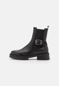 Bottines noires en cuir avec un bout rond, des panneaux élastiques sur les côtés, un accent de boucle et un petit talon épais. Texture lisse et semelle robuste.