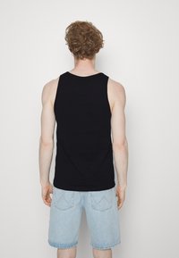 Débardeur noir sans manches en coton, avec un col rond et une coupe décontractée, associé à un short en jean bleu clair avec des poches.