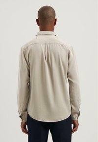 Hellbeige Langarmhemd mit klassischem Kragen, geknöpften Manschetten und abgerundetem Saum. Der Stoff wirkt weich mit einer dezenten Textur.