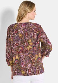 Bunte, gemusterte Bluse mit Dreiviertelärmel, Rundhalsausschnitt und einem lockeren Design, das floral und paisley Muster in verschiedenen Lila- und Rosatönen zeigt.