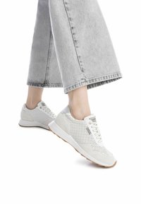 Zapatillas blancas perforadas con acentos grises, cierre de cordones y suela beige, combinadas con pantalones de mezclilla de pierna ancha en gris claro.