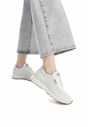 Zapatillas blancas perforadas con acentos grises, cierre de cordones y suela beige, combinadas con pantalones de mezclilla de pierna ancha en gris claro.