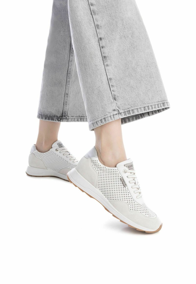 Zapatillas blancas perforadas con acentos grises, cierre de cordones y suela beige, combinadas con pantalones de mezclilla de pierna ancha en gris claro.