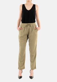 Top nero senza maniche con scollatura a V profonda, abbinato a pantaloni larghi di un leggero verde oliva con cintura elastica e tasche laterali.