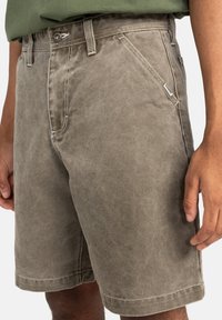 Shorts in cotone beige con una vestibilità rilassata, passanti per cintura, tasche laterali e dettagli di cucitura a contrasto. Il tessuto ha una finitura morbida e testurizzata.