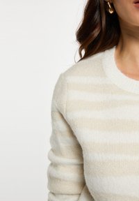Suéter a rayas crema y beige con un tejido suave y texturizado y un cuello redondo acanalado. Un sutil brillo en las rayas añade un detalle extra.