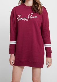 Bordeaux-huppari mekko pitkillä hihoilla, ribbireunuksilla, valkoisilla raidoilla hihoissa ja "Tommy Jeans" -logo kauniilla käsialalla rinnassa.