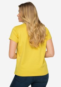 Geel T-shirt met korte mouwen en een ronde hals, gemaakt van zachte, gladde katoen. Van achteren gezien heeft het een rechte zoom en een getailleerde pasvorm.