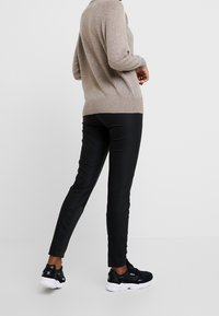 Pull en tricot beige à manches longues, associé à un pantalon noir slim et des chaussures de sport noires à semelles blanches.