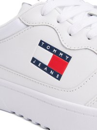 Sapatilhas brancas com um cabedal em couro texturizado, apresentando um proeminente logótipo da Tommy Jeans em vermelho e azul na lateral. Fecho com atacadores.