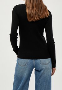 Svart ribbad tröja med långa ärmar, åtsittande design och rundad halsringning, i kombination med högmidjade blå denimjeans.