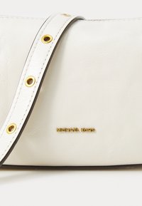 White leather handbag featuring a textured surface, gold hardware accents, and a strap with circular cutouts. Brand logo is embossed in gold.