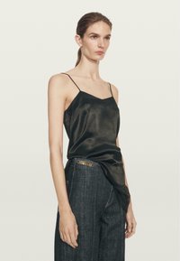 Czarna satynowa koszulka na ramiączkach z cienkimi paskami, dekoltem w kształcie litery V i luźnym krojem, w zestawieniu z ciemnoniebieskimi dżinsami z wysokim stanem ozdobionymi guzikami.