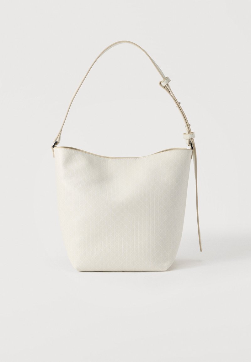 Λευκή τσάντα ώμου από λείο υλικό με διακριτικό μοτίβο διαμαντιού. Διαθέτει έναν ρυθμιζόμενο ιμάντα και στρογγυλεμένο πάνω μέρος.