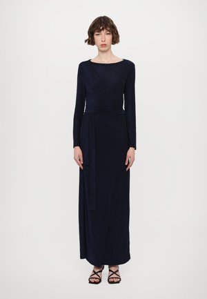 Navy blue lange mouw jurk in een wikkelontwerp, gemaakt van sprankelende stof. Voorzien van een tailleband en reikt tot de enkels, gecombineerd met strappy schoenen.