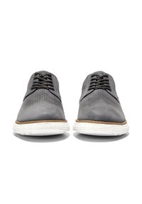 Zapatos de cuero gris con detalles perforados, cordones negros y una suela blanca con un acento marrón. Diseño clásico, forma elegante, estilo casual.