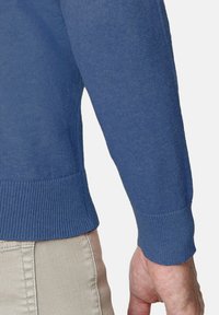 Jersey azul de punto, con un escote y puños acanalados, de textura suave y silueta ajustada. Pantalones en un tono beige claro a juego.