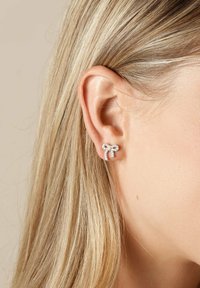 Silverörhängen formade som en båge, prydda med små klara rhinestones, synliga mot en ljusbeige bakgrund och bärs i ett hål i örat.