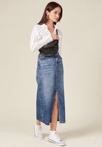 Denim maxi-jurk met een voorkneeling, in een vervaagde blauwe was. Gepaarde met een witte blouse met knopen en witte hoge sneakers.