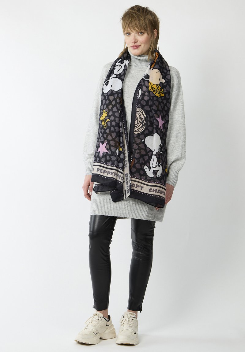 Écharpe noire avec des personnages de bande dessinée colorés, des motifs et une bordure décorative. Portée sur un pull gris clair et des leggings noirs.