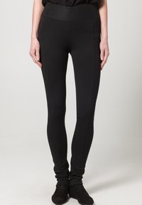 Zwarte leggins van rekbaar, zacht materiaal met een brede elastische tailleband en een slim fit, met een gladde textuur en zonder zichtbare patronen.