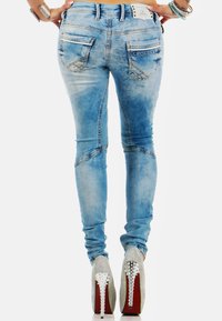 Dunne denim jeans in lichtblauwe wassing met vervaagde accenten, decoratieve stiksels en twee achterzakken. Draagt met zilverkleurige versierde hakken.