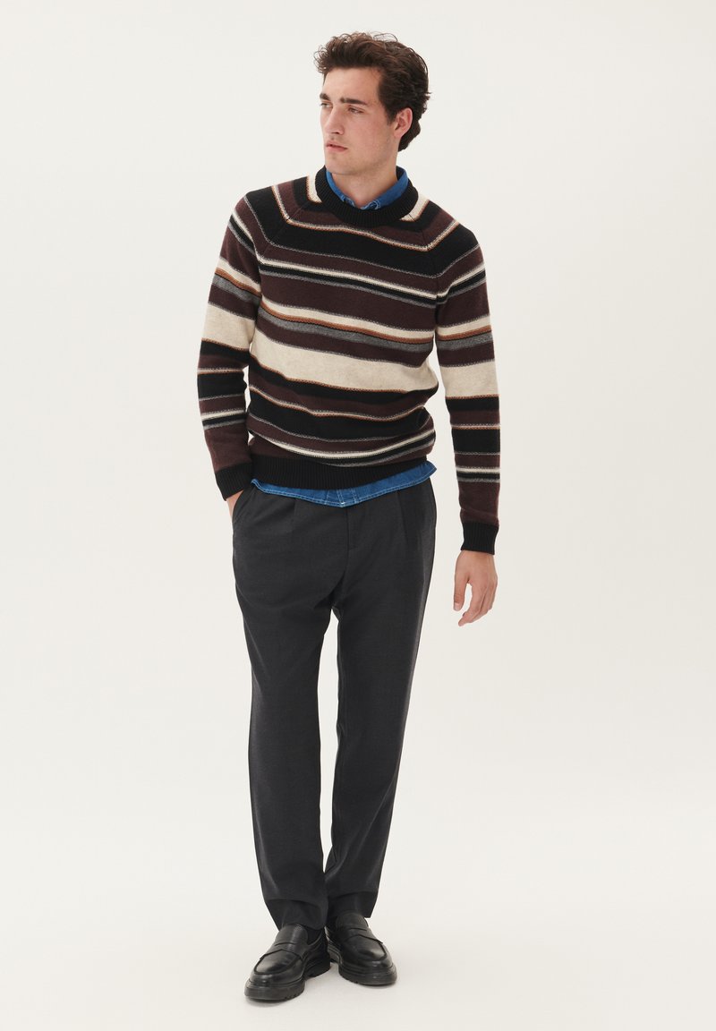 Maglione lavorato a maglia con righe orizzontali in marrone, crema e ruggine. Indossato sopra una camicia blu con pantaloni scuri e mocassini neri.