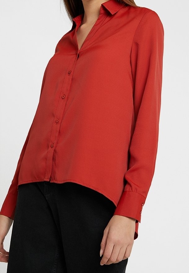 Blouse rouge à manches longues avec devant boutonné, col et ourlet légèrement arrondi. Fabriquée en tissu léger à texture lisse.