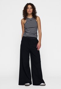 Pantaloni larghi neri abbinati a un top senza maniche a righe bianco e nere. L'outfit presenta un design rilassato e una texture morbida.