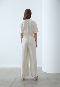 Beige jumpsuit med kortermede og elastisk midje, med bred ben design og et lett, teksturert stoff.