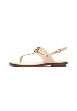 Sandalias planas beige con bucle para los dedos, una correa ajustable en el tobillo y un acento de hebilla en tono dorado. Parte superior de cuero suave y suela plana.