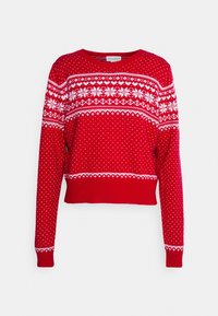 Pull en tricot rouge à manches longues, avec des motifs de flocons de neige blancs et des pois. Conception raccourcie avec des poignets et un ourlet côtelés.