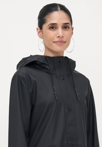 Black waterproof jacket with a hood, featuring snap buttons, adjustable drawstring, and side pockets. Smooth texture, minimalistic design.