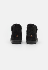 Bocanci gri din suede cu talpă din cauciuc negru, având un logo portocaliu "Z" și o curea în jurul gleznei pentru ajustare.