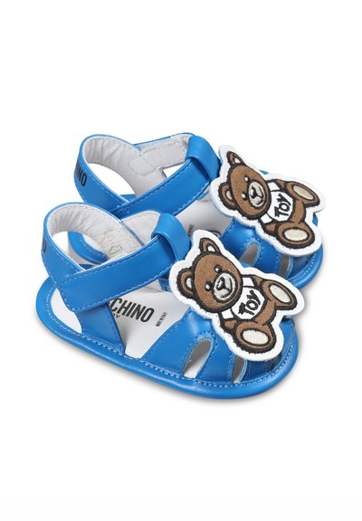 Sandales en cuir bleu avec plusieurs découpes, des sangles ajustables et une appliqué en peluche de ours en peluche sur le bout. Doublure intérieure blanche.