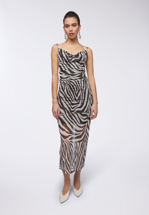 Abito aderente e trasparente con strisce a zebra in bianco e grigio, scollatura a cowl e spalline regolabili, abbinato a tacchi bianchi con punta.