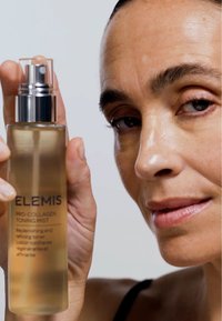 Klar glassflaske med en sølv spraydyse, som inneholder lys amber toningsmist. Etiketten leser "ELEMIS Pro-Collagen Toning Mist."