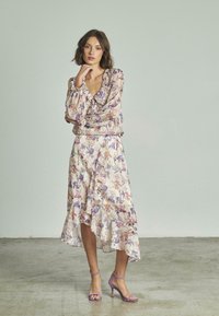 Blumenkleid aus weichem Stoff mit Rüschendetails, das in lila und rosa Mustern gestaltet ist. Kombiniert mit passenden lavendelfarbenen High Heels.